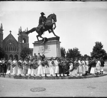 J.E.B. Stuart Monument on Monument Avenue. Stuart is on his horse looking backward. There is a school group of young women circling the statue all carrying flowers or flowered wreaths for a Memorial Day celebration. The girls are from the Collegiate School for Girls. May 1917.