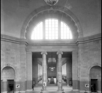 Waiting room in Broad Street Train Station. Two large ionic columns and four long wooden benches. A globe hangs above and the ceiling is tall.
