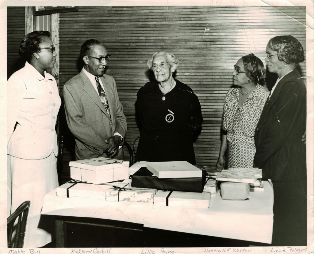 Lillian Payne stands in the center wearing a black dress. Two Black woman are to her right and another Black woman and a Black man are to her left. All are looking in her direction.