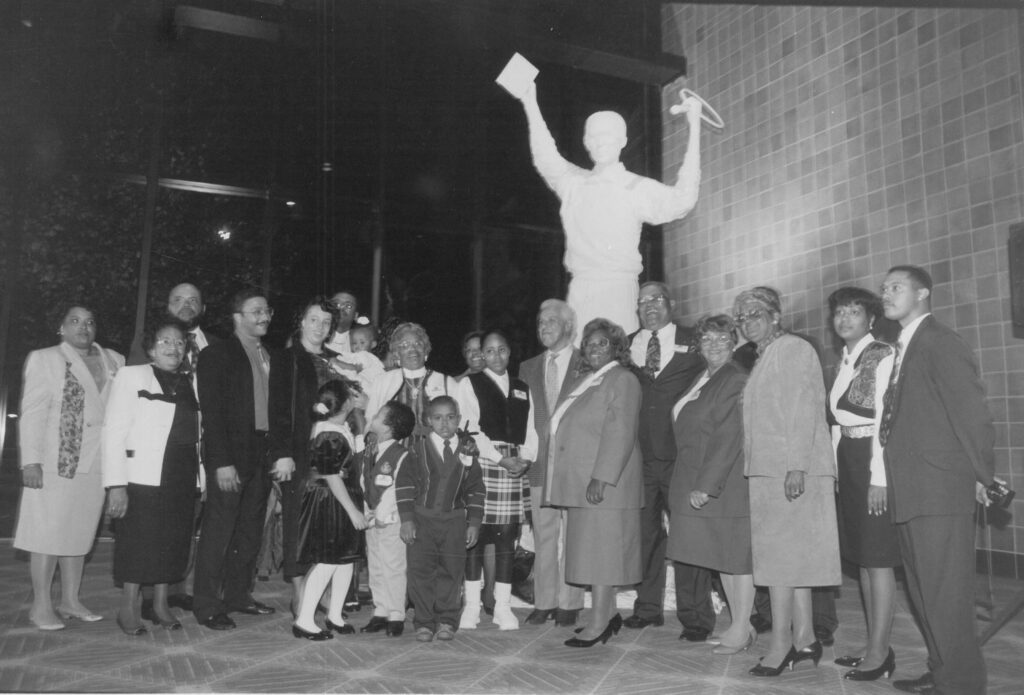 A group of people standing in front of a white statue of Arthur Ashe.