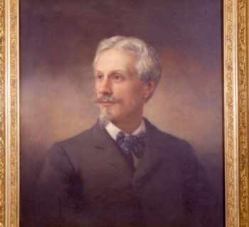 Portrait of the artist Edward V. Valentine as middle-aged man; face is oriented three-quarters to left; dark gray jacket, full bow tie, blue with white polka-dots; brown eyes; hair is center parted, almost white, gray mustache and long narrow goatee; gray background.
