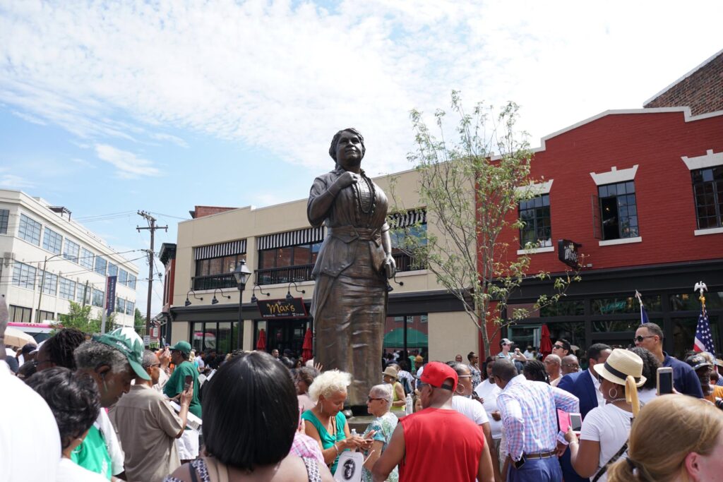 Bronze statue of Maggie L. Walker with a crowd surrounding her at the dedication.