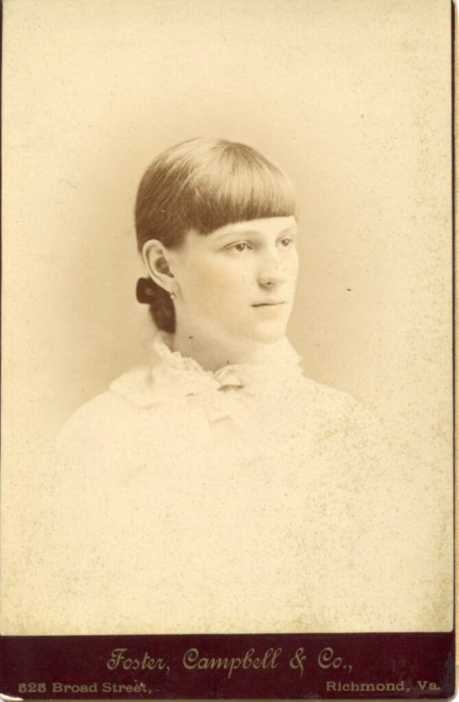 Picture of a young white woman in a white shirt looking to the side. Her brown hair is pulled away from her face.