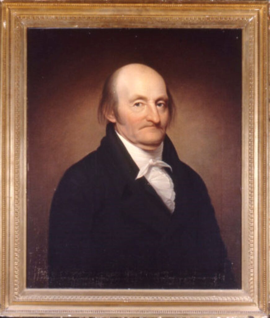 Portrait of Dr. James McClurg with a golden frame. He is wearing a black coat with a high collared shirt tied around his neck. He is predmoniately bald with deep set eyes.