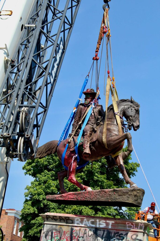 Painted covered equestrian statue of J.E.B. Stuart being lifted by ropes, pulleys, and a crane in Richmond in 2020.