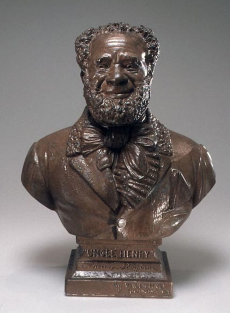 Plaster bust painted brown of a Black man, smiling with a beard, wearing a formal coat and neck tie.