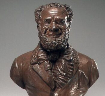 Bronze bust of a well-dressed African American older man with a full beard. He is smiling. Inscription reads 