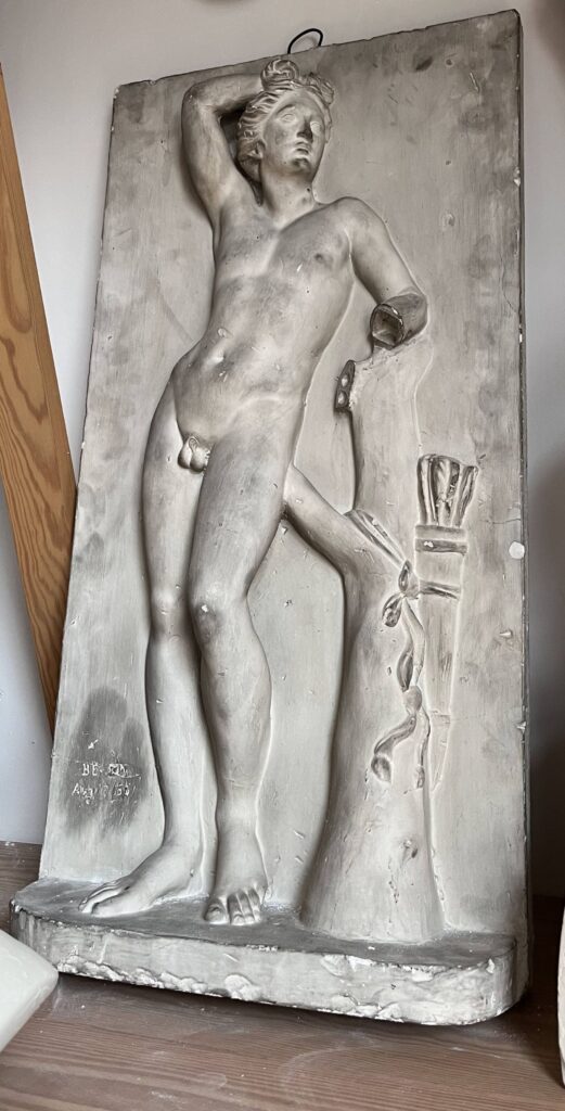 Edward Valentine’s copy of Apollino, a plaster plaque with a young nude male leaning on a tree stump.