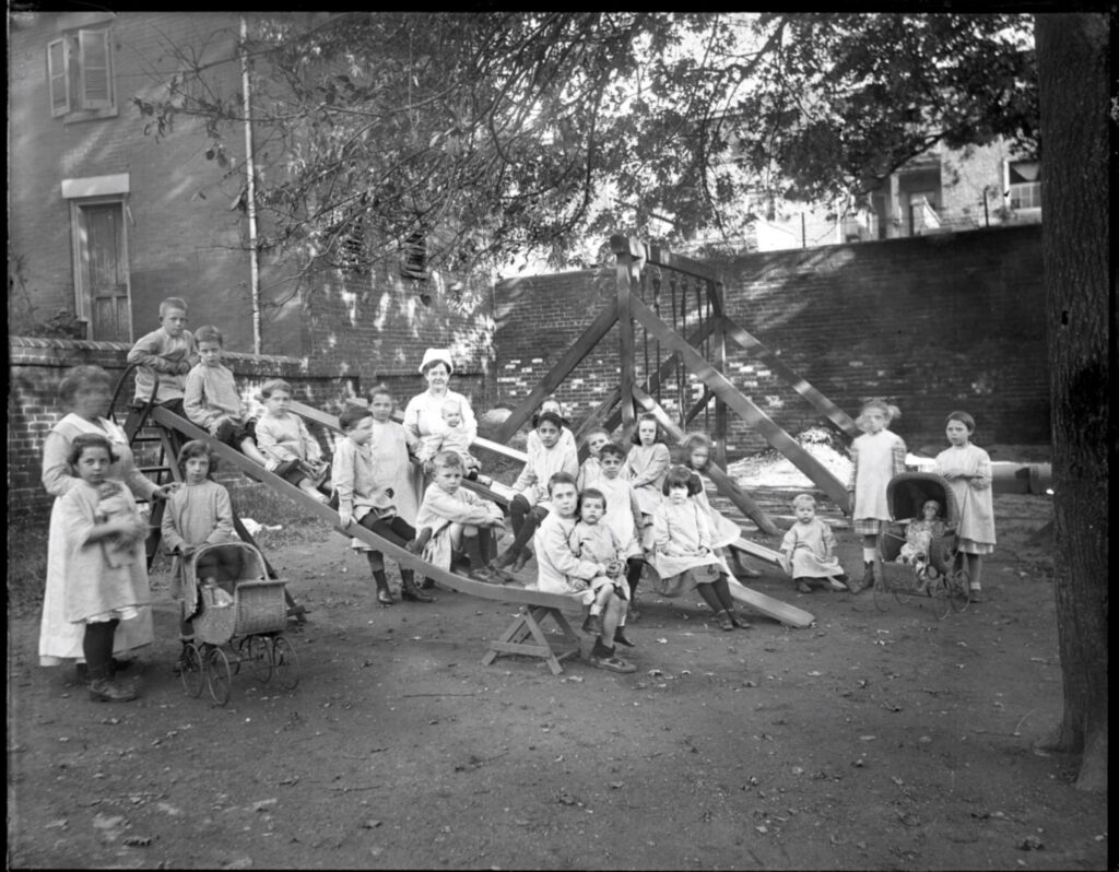 Children (all white) playing on a playground enclosed by brick walls.