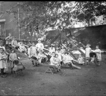 Children (all white) playing on a playground enclosed by brick walls.