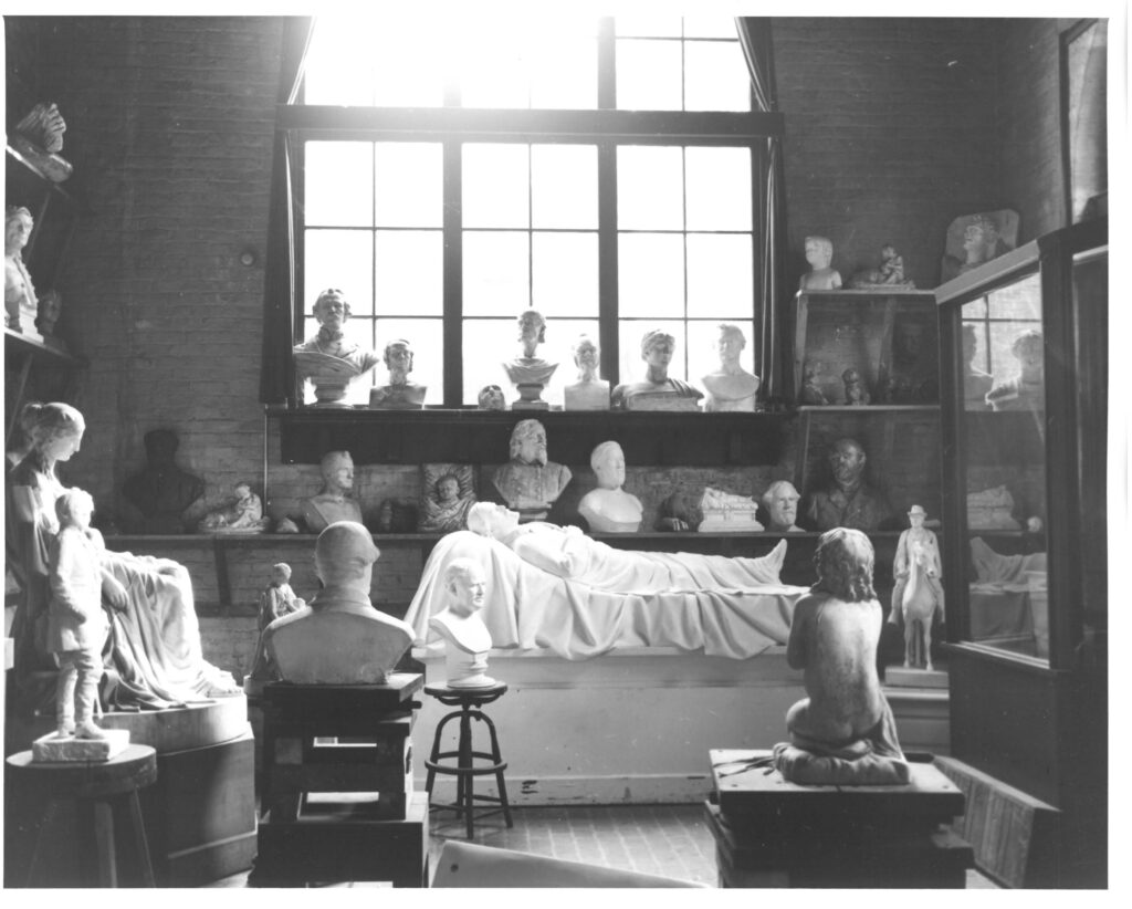 View of the Valentine Studio with sculptures in the foreground and along the walls of the space with a large, arched window in one wall.