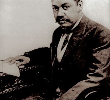 Portrait of a middle-aged Black man in a suit with his right hand on his typewriter.