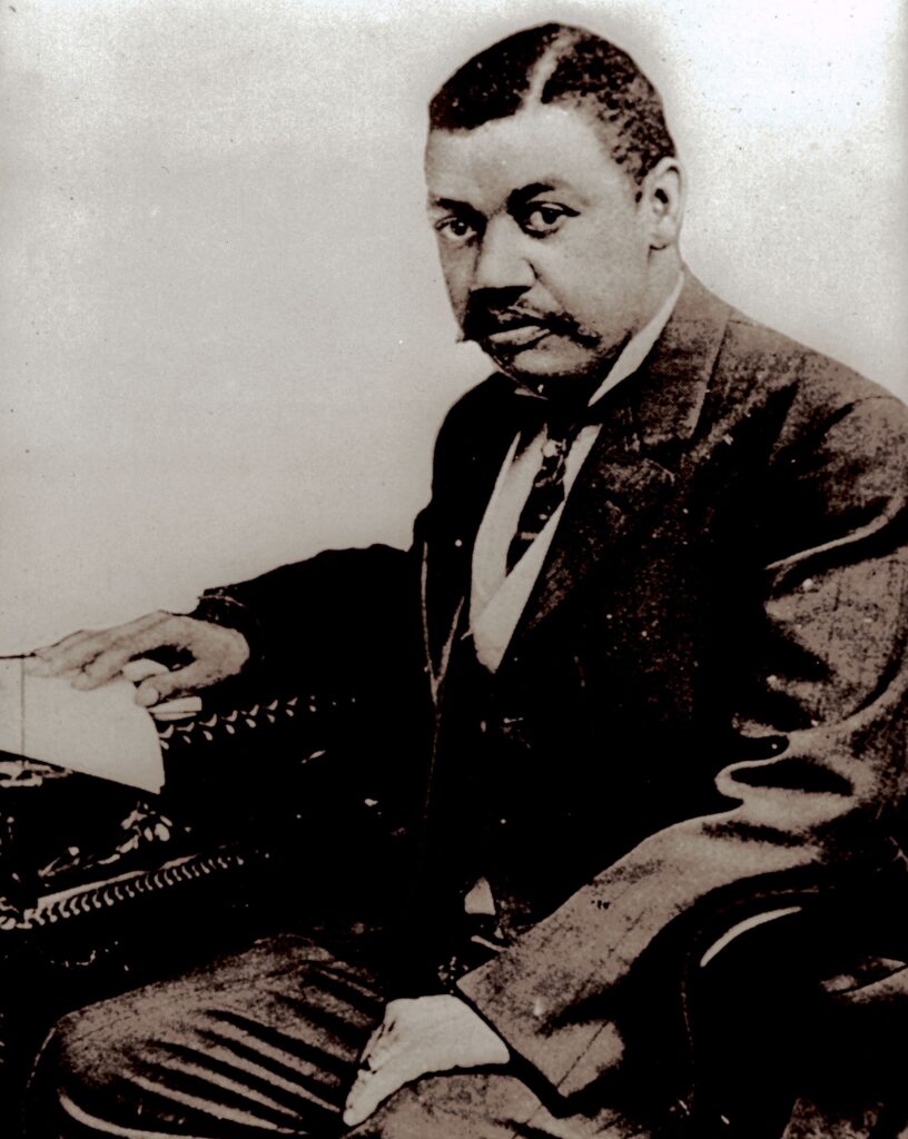 Portrait of a middle-aged Black man in a suit with his right hand on his typewriter.