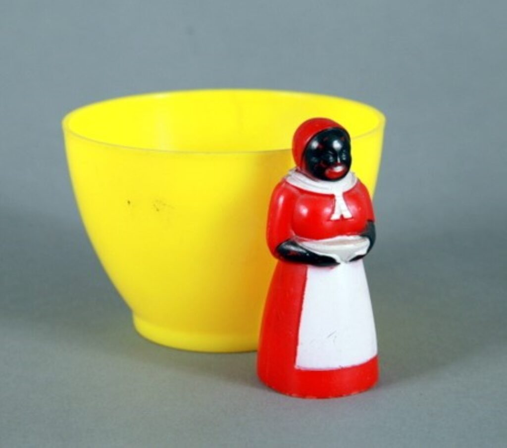A yellow ceramic bowl with a handle depicting a Black woman in a red cap and dress with a white apron.