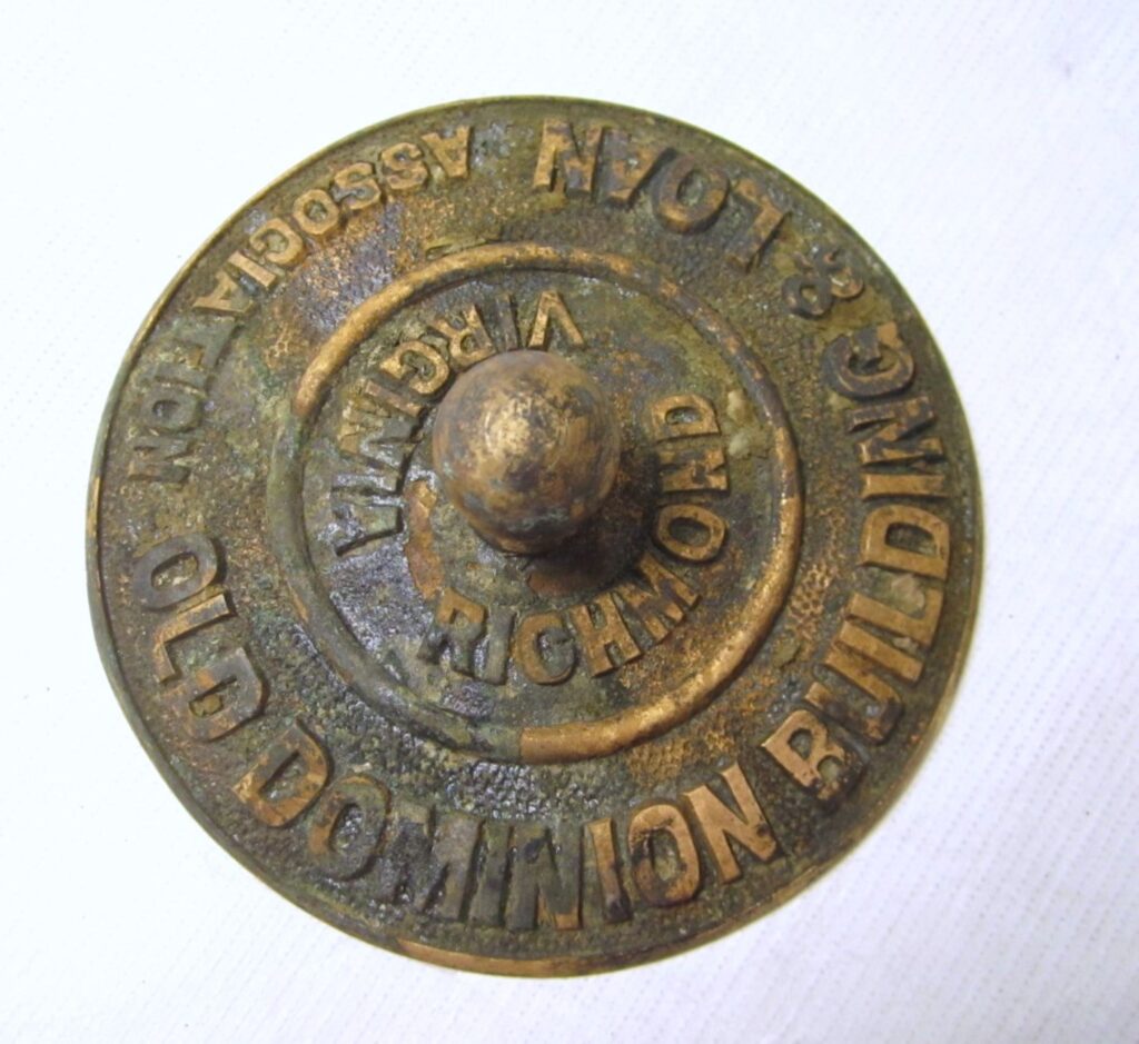 Round bronze object with a nub handle reading “Old Dominion Building & Loan Association” and “Richmond Virginia” in the round.