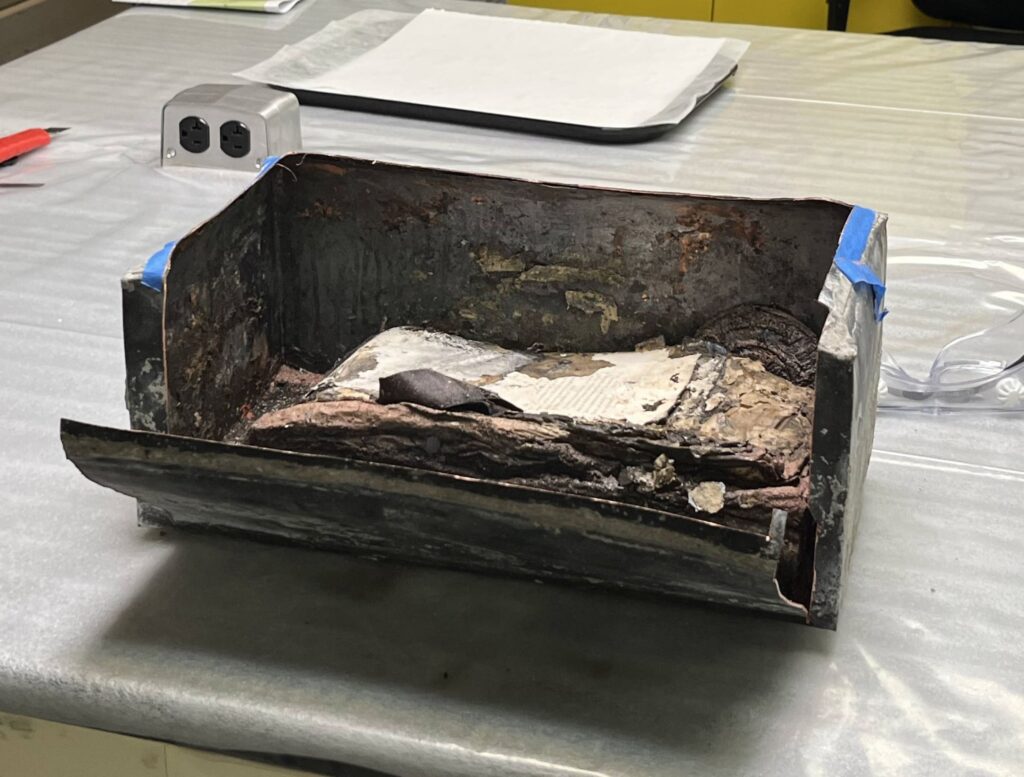Metal box with the top removed and front cut open revealing stacks of wet paper items