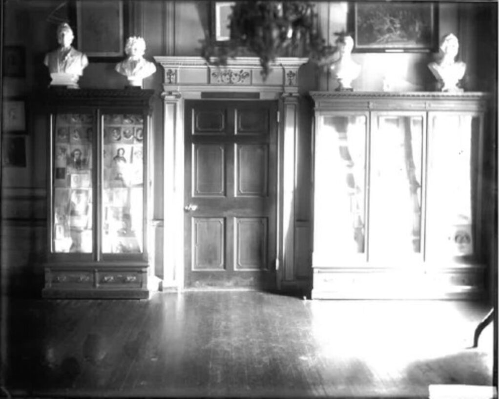 View of the early Valentine Museum glass cases filled with prints with busts on top of them and a door in between the cases.