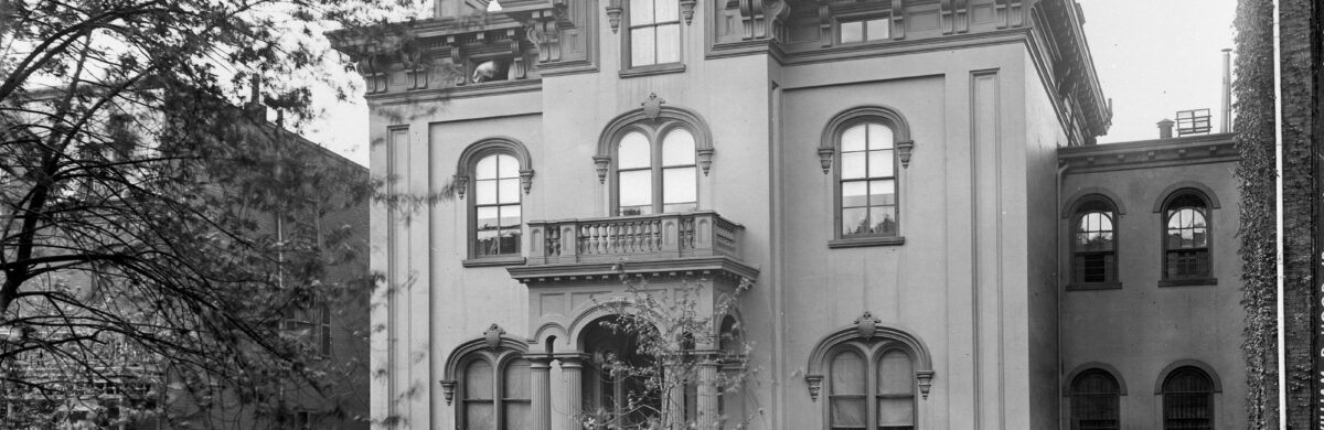 Large three-story home with front portico with double columns. There are ten arched windows on the front side.