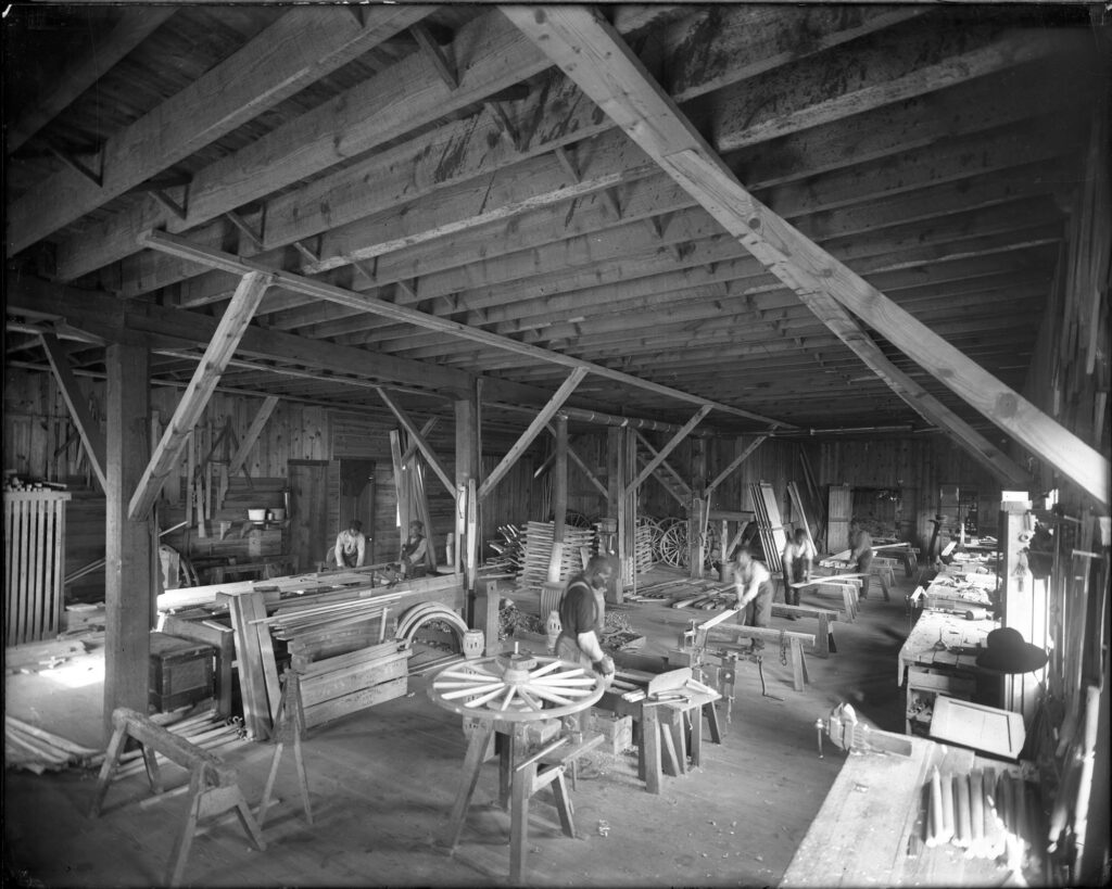The wagon making shop at St. Emma Industrial & Agricultural Institute at Belmead Plantation, Powhatan County, near Richmond; image shows young Black men working with boards and saws in a large, open room.