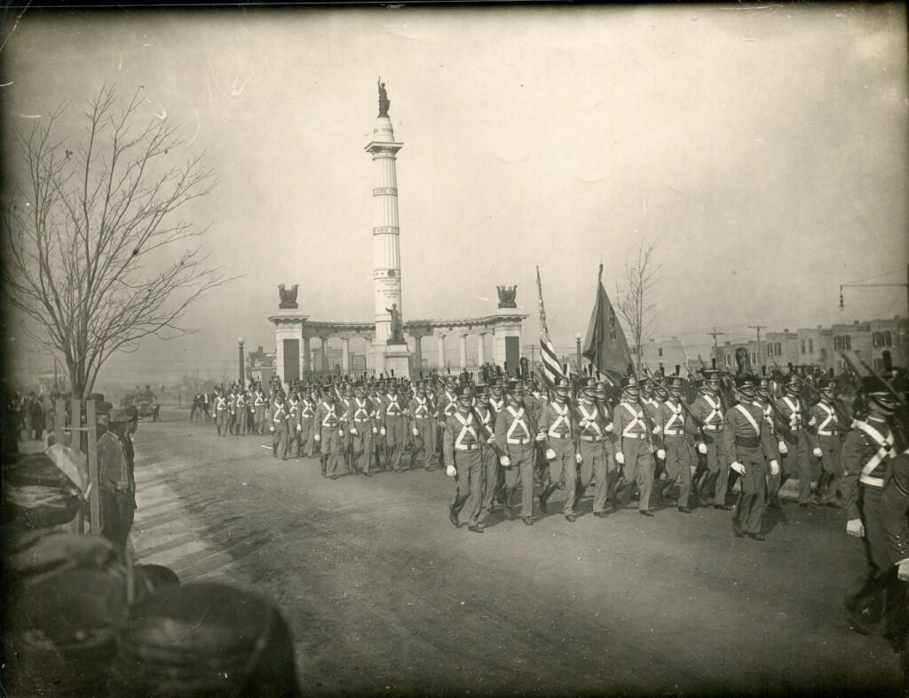 Rows of Confederate veterans dressed in uniforms marching in a parade in front of the Jefferson Davis Monument on the day of its unveiling.